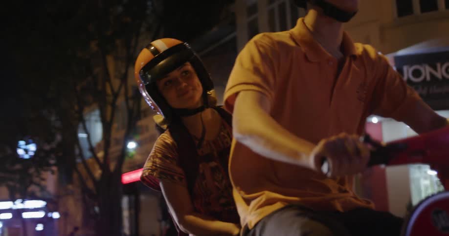 Man and woman ride a scooter on a city street