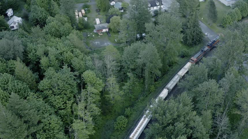 A train travels through the forest and a small town - 4K Aerial