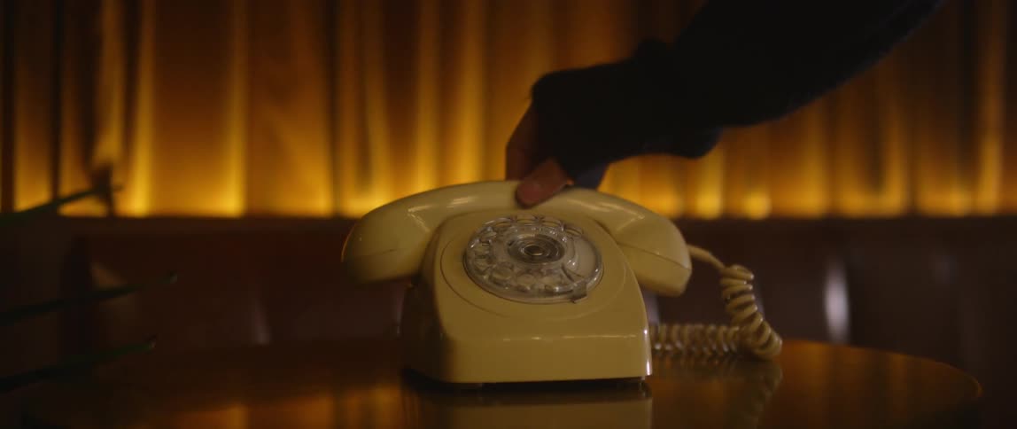 A person answers a rotary phone on a table