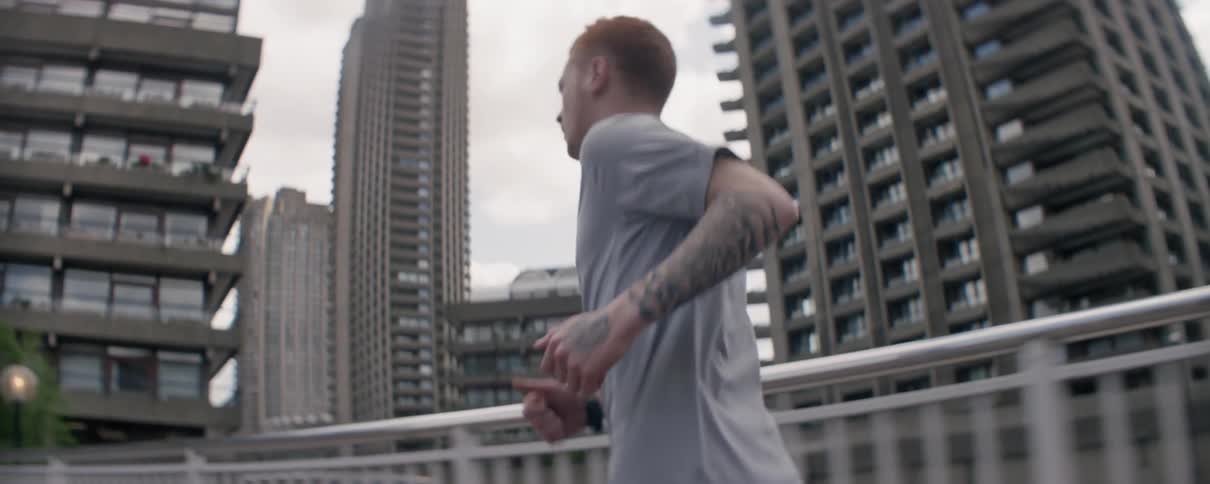 A man stumbles as he's jogging across a pedestrian bridge in a city