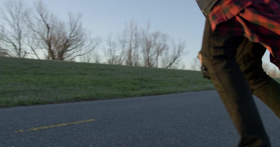 A man rides a skateboard down the street at sunset