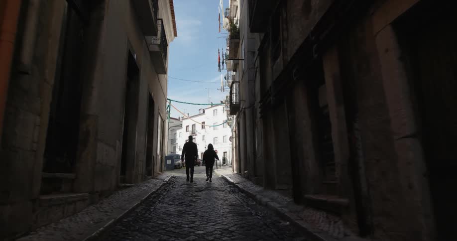 Two people walk down an alleyway in a city on a sunny day