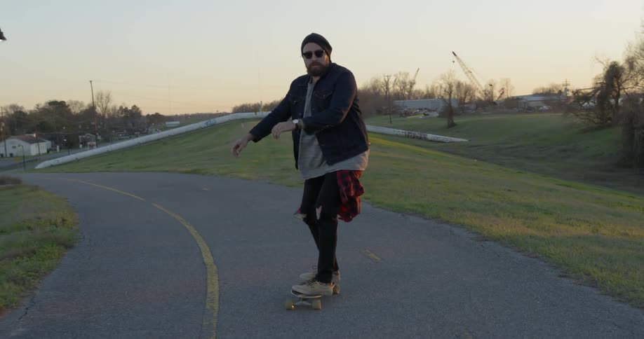 Man wearing sunglasses rides a skateboard on the road