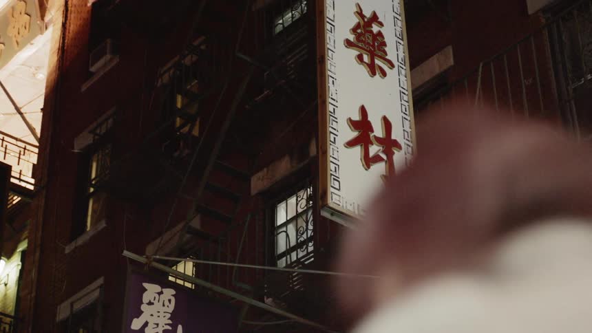 A asian sign and banner hang from a brick building with a fire escape