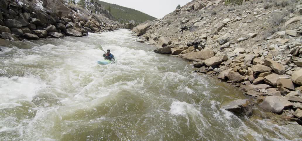 A person kayaks through white water and past rocks in a river
