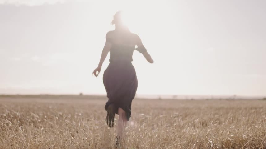 Woman in a skirt runs through a field under a cloudy sky