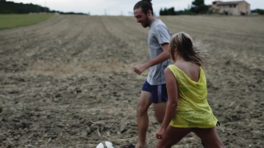A man and woman play with a soccer ball in a field