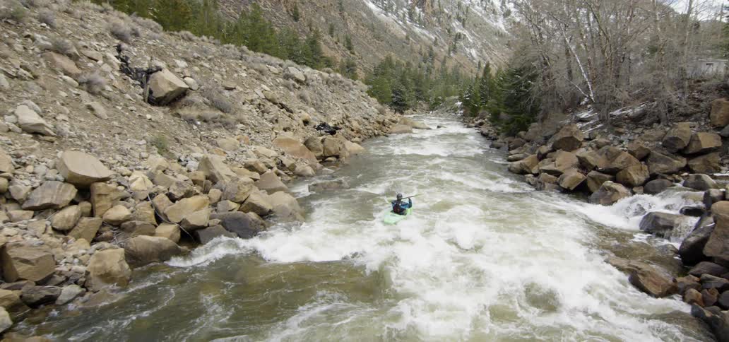 Man in a kayak paddles down the rough water in a creek