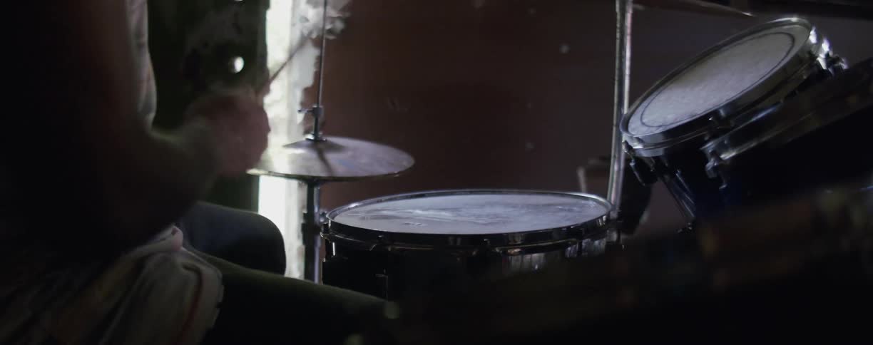 A man is playing drums inside during the day