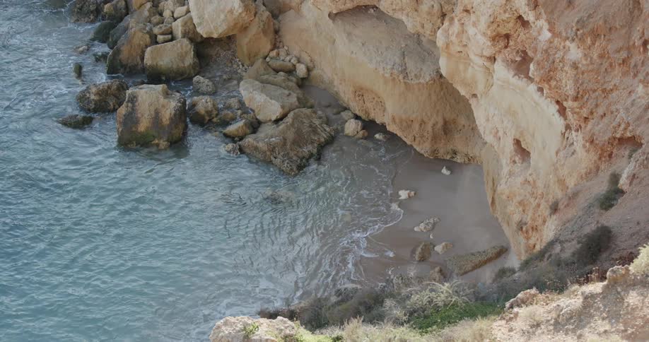 Water is lapping the shores of beach beneath cliffs in sunlight