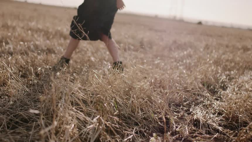 Woman in a black dress and black boots walks in a field