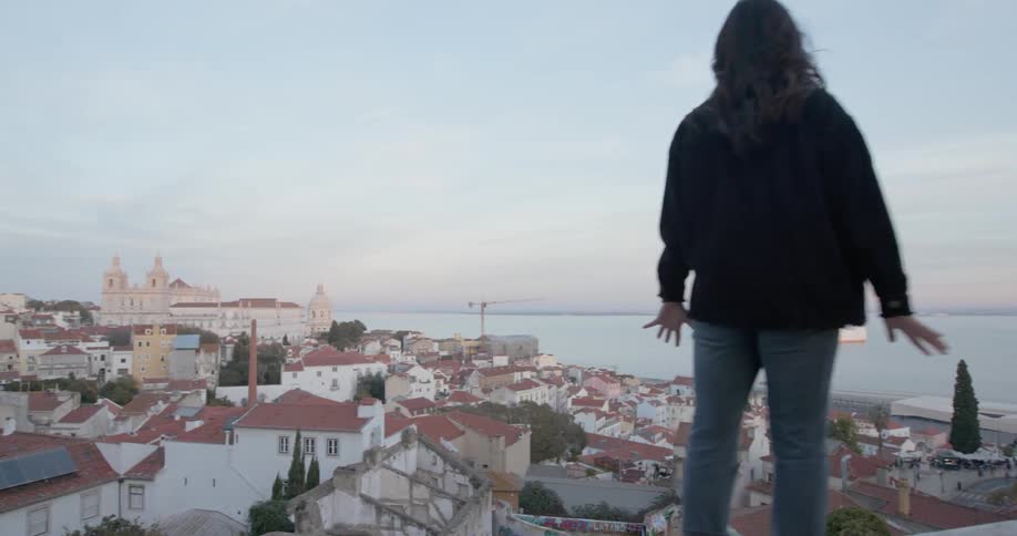 Woman walks on ledge overlooking oceanside city