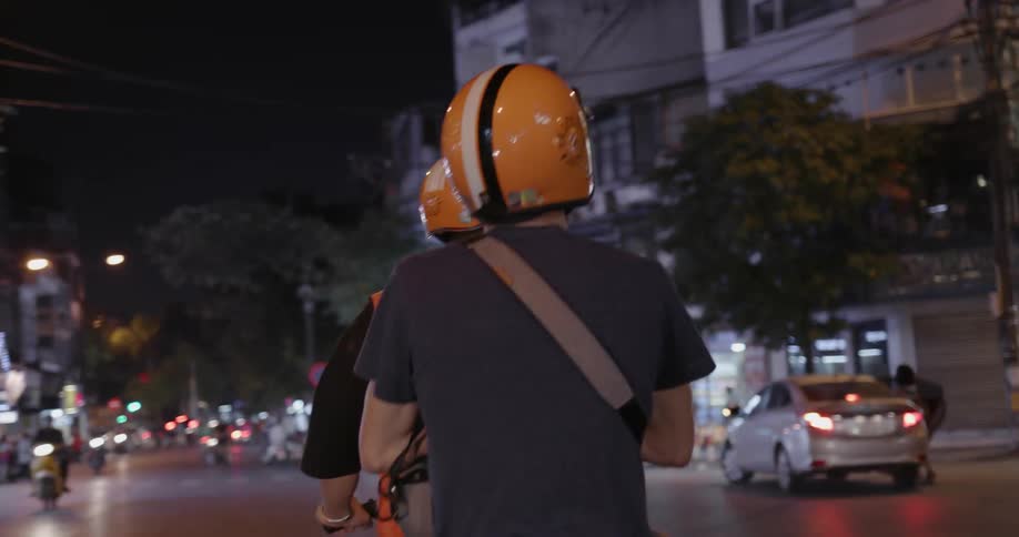Two people ride a scooter down the street at night