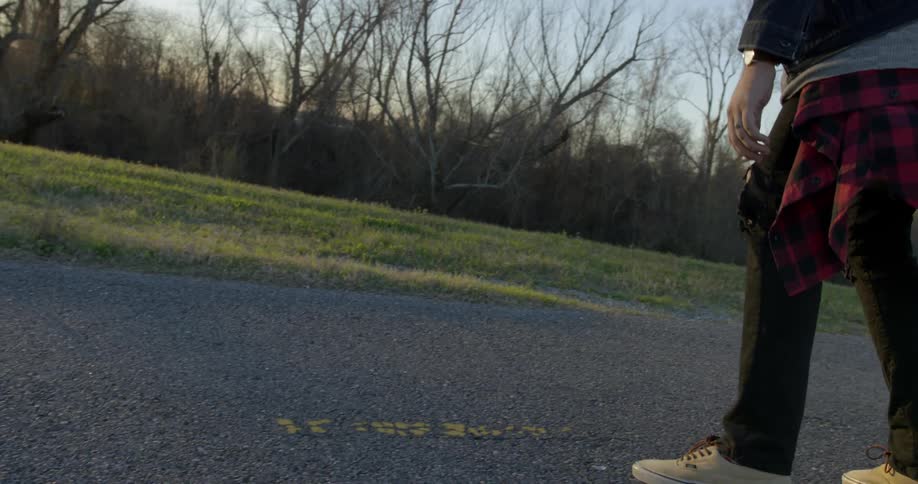 Man skateboards on a rural road at sunset