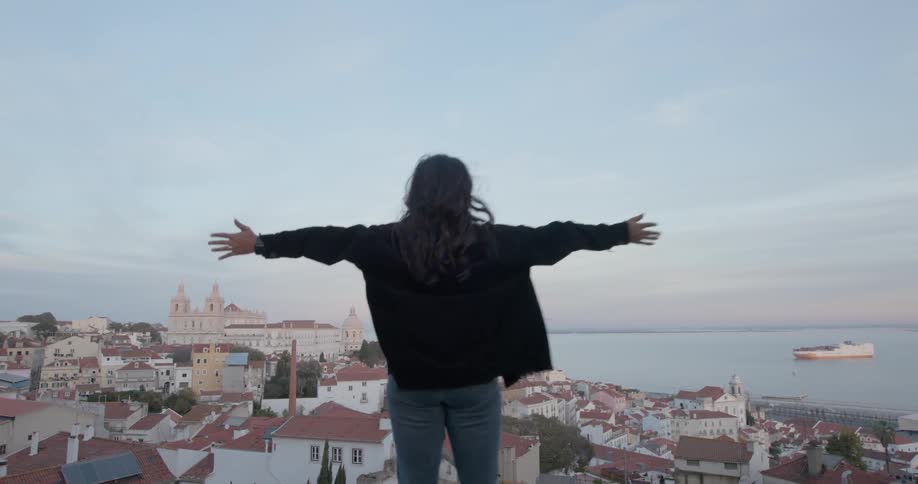 Woman stands with her arms outstretched overlooking a coastal town