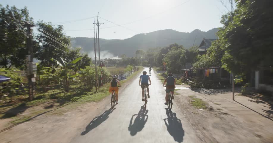 Three people ride their bikes down a country road on a sunny day