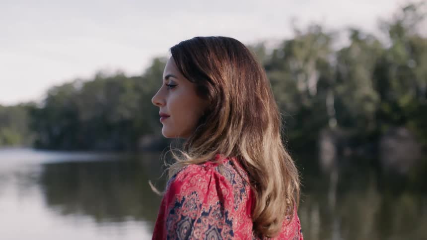 A woman stands by a lake looking to the side