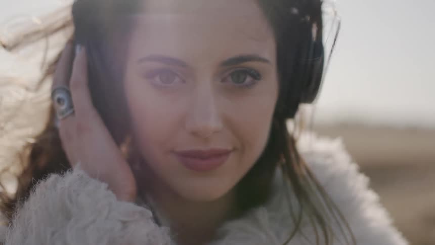 The woman is outside on a windy day listening to headphones