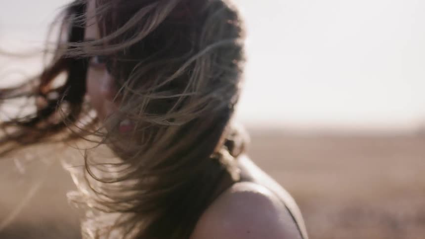 Woman smiles while standing in a field on a windy day