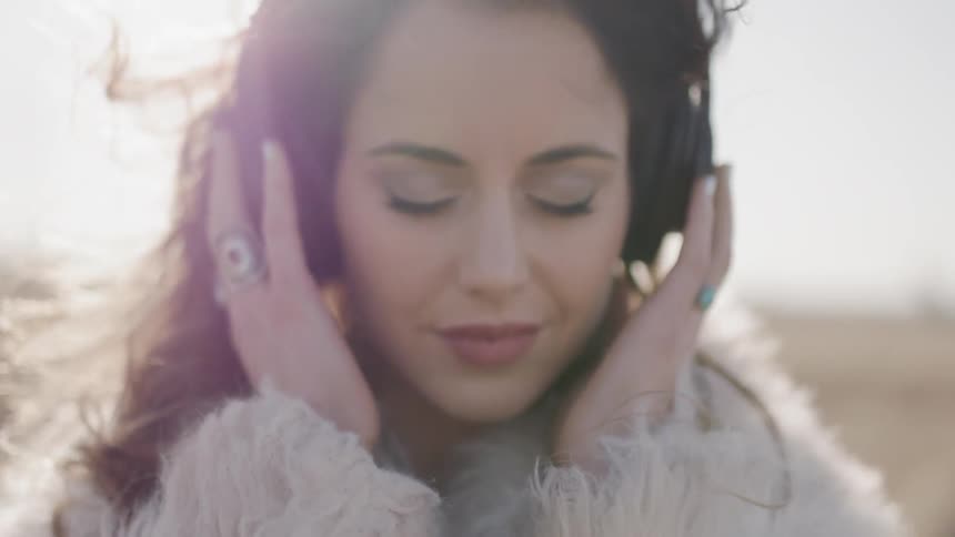 Woman touches the headphones over her ears as she stands under the bright sun