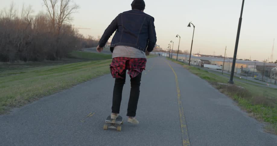 Man skateboards on a road at sunset