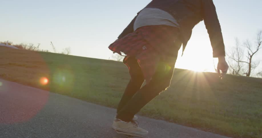 Man skateboards on a rural road at sunset