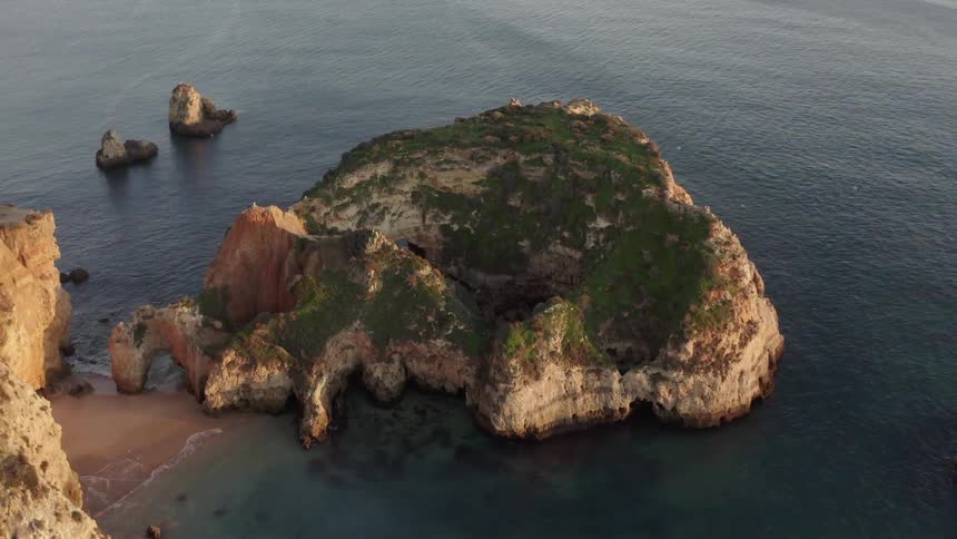 Large moss covered rock sits in the ocean