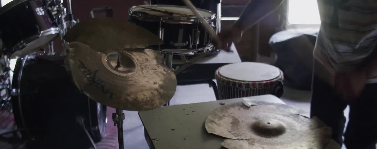 A man is drumming on cymbals as he stands inside in daylight