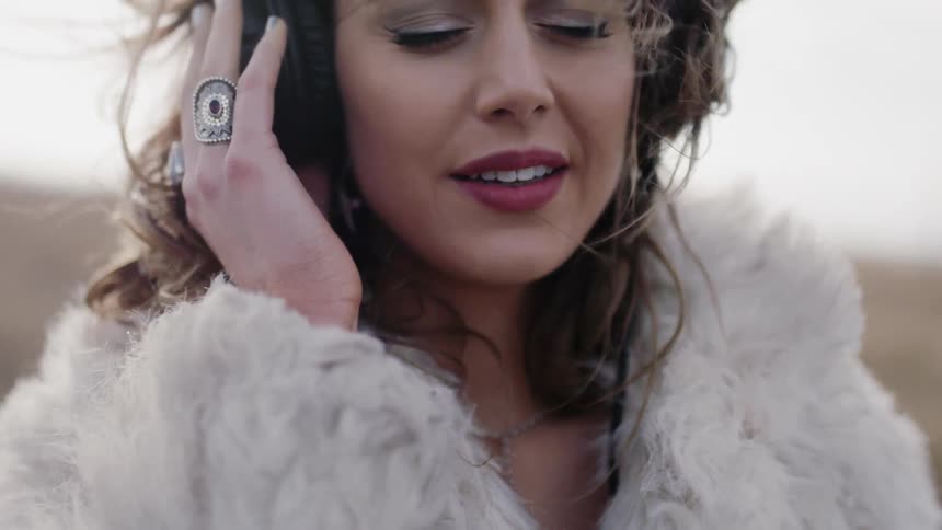 A woman is listening to headphones on a windy field