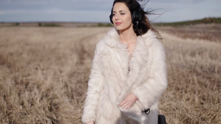 A woman is swaying as she listens to music outside in a field on a cloudy day