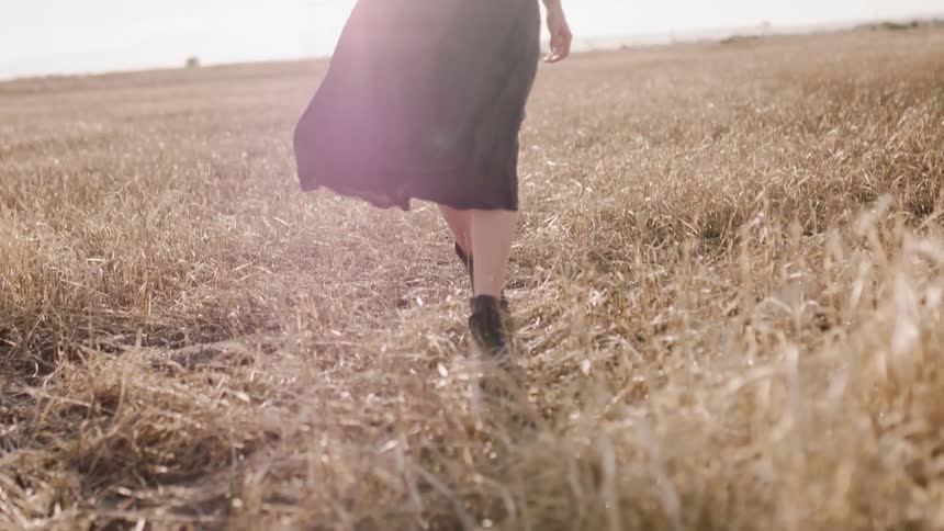 A woman wearing a dress walks through a field on a sunny day