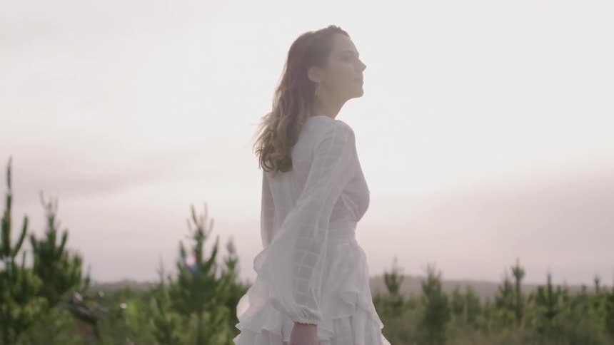 The wind blows a woman's white dress as she walks in a field