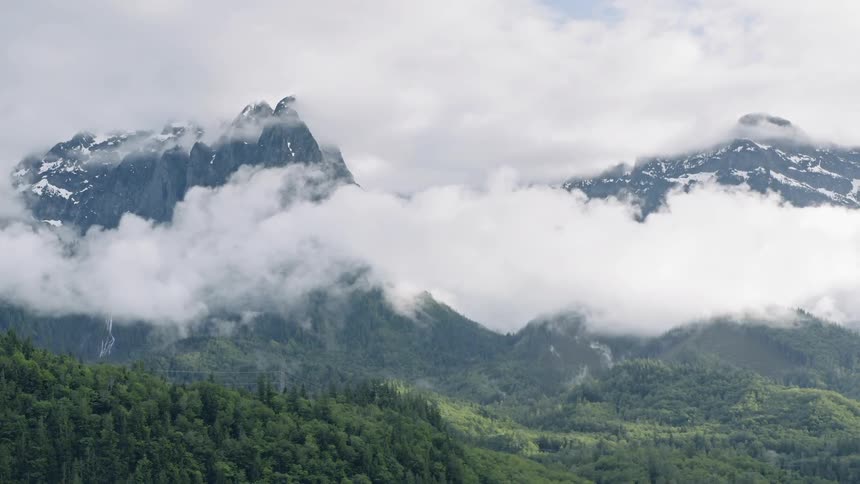 Clouds float around tall mountains - 4K Aerial
