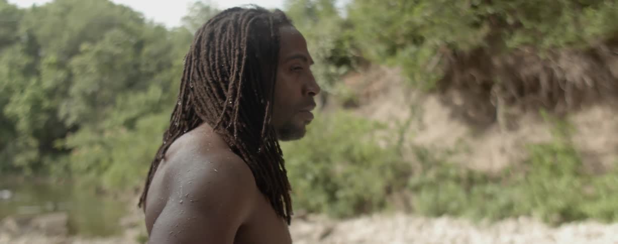 A man standing outside without a shirt turns around
