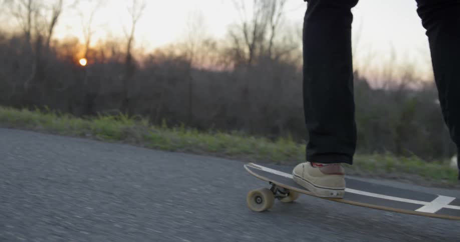 Man skateboards on a rural road at sunset