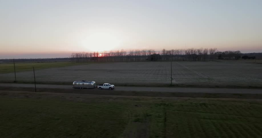 Truck pulling travel trailer is driving on country highway at sunset
