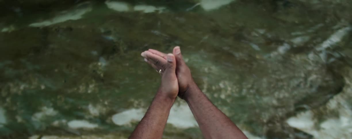 Man wiggles his hands above a flowing stream