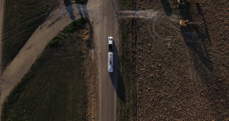 Truck drives down a country road pulling a silver trailer