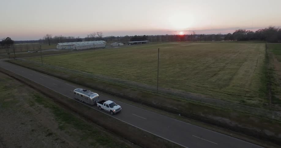 Truck pulling travel trailer is driving on country highway at sunset