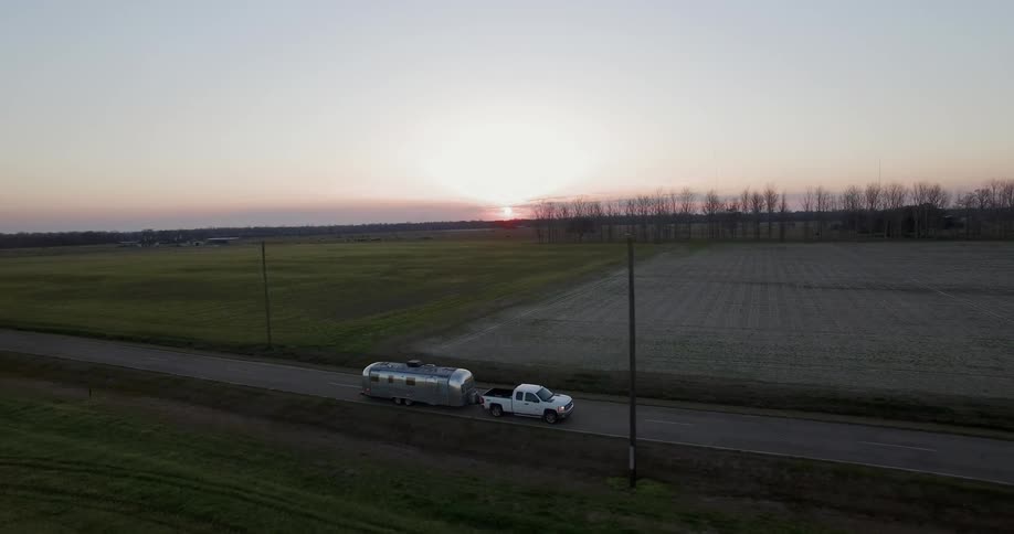 Truck pulls a trailer on a rural road at sunset