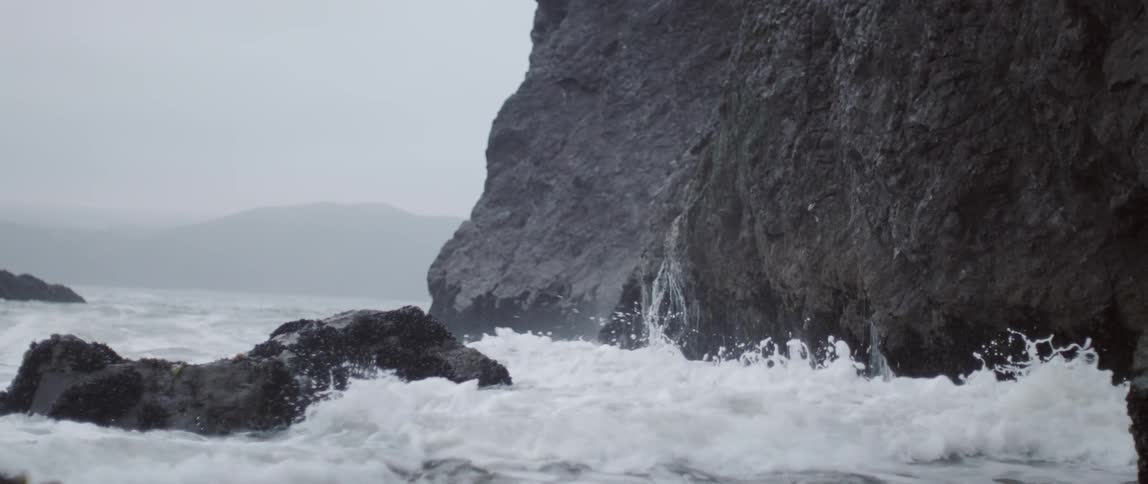 The large waves crash against the rocks on the shore