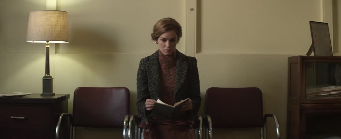 A woman sits in a waiting room holding a book until she's called away