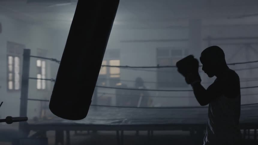A man punches the heavy bag in the dark gym