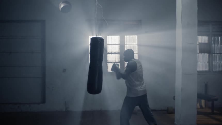 Man is boxing a punching bag in front of sunny window