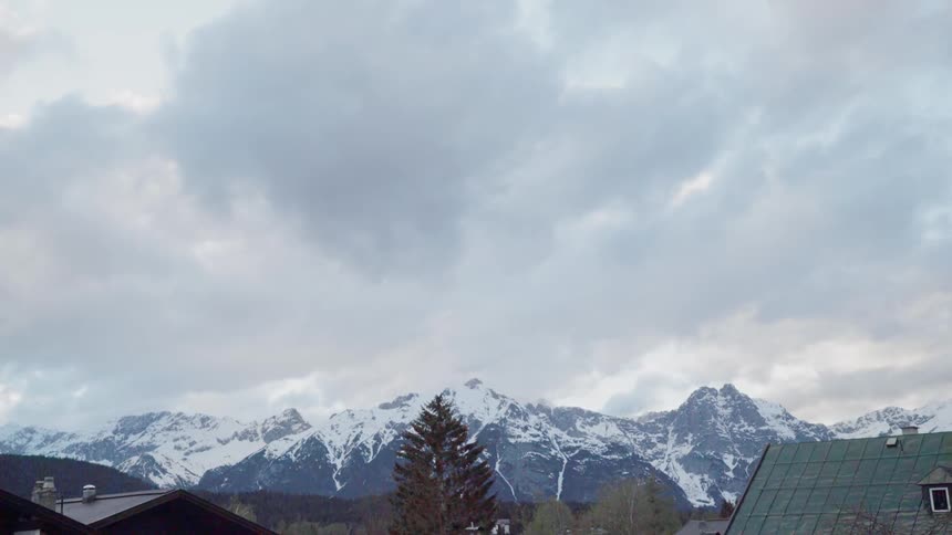 Clouds are drifting over snow-covered mountains beyond cabins during the day