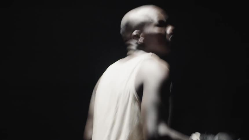 A man wearing boxing gloves is surrounded by darkness and turning in circles