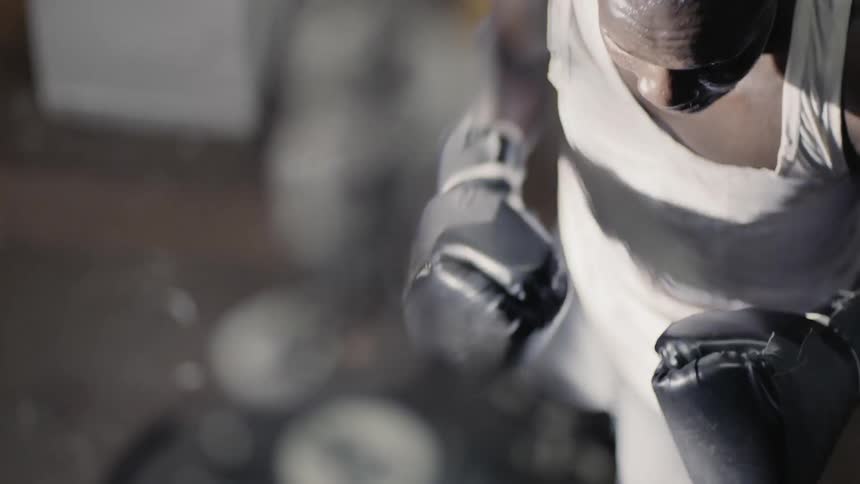 A man with boxing gloves on energetically punches a heavy bag