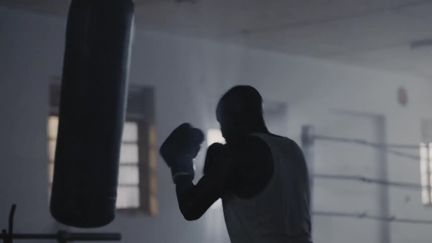 A man wearing boxing gloves hits the heavy bag in a gym