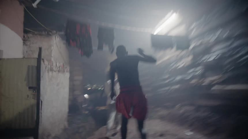 Boys run through a village  pushing laundry out of the way