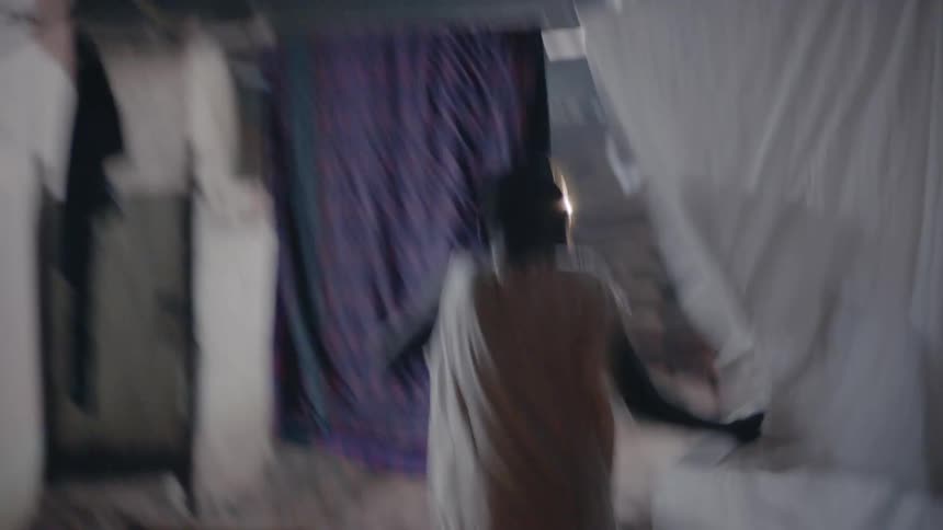 A boy running through a village at night pushes laundry on the line aside